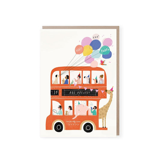 A white card with a red double-decker no. 10 bus in on it. The words ALL ABOARD are written in the black space under the top windows and "the party bus" is written between the wheels on the side of the bus. The bus has a dog holding a bunch of colourful balloons which are floating above the bus, there are people, an elephant wearing a party hat and a man pulling a party popper. A giraffe is standing on the open platform at the back of the bus holding pink bunting a bird is holding the other end.