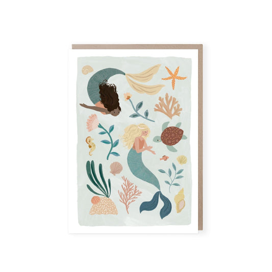 A water colour sea green card with a white border. Card features two mermaids, one fair skinned with blonde hair and one dark skinned with black hair swimming amongst sea foliage, a conche shell, coral,  a turtle and a sea horse. Comes with a brown kraft envelope