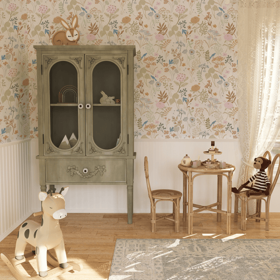 A Vintage style playroom corner with a bamboo kids table and 2 chairs, and a vintage green wardrobe on tall legs. Wall is panelled in white up to a third up with our Dreamy Floral Wallpaper above. Wallpaper features muted leaves and florals on a white background.