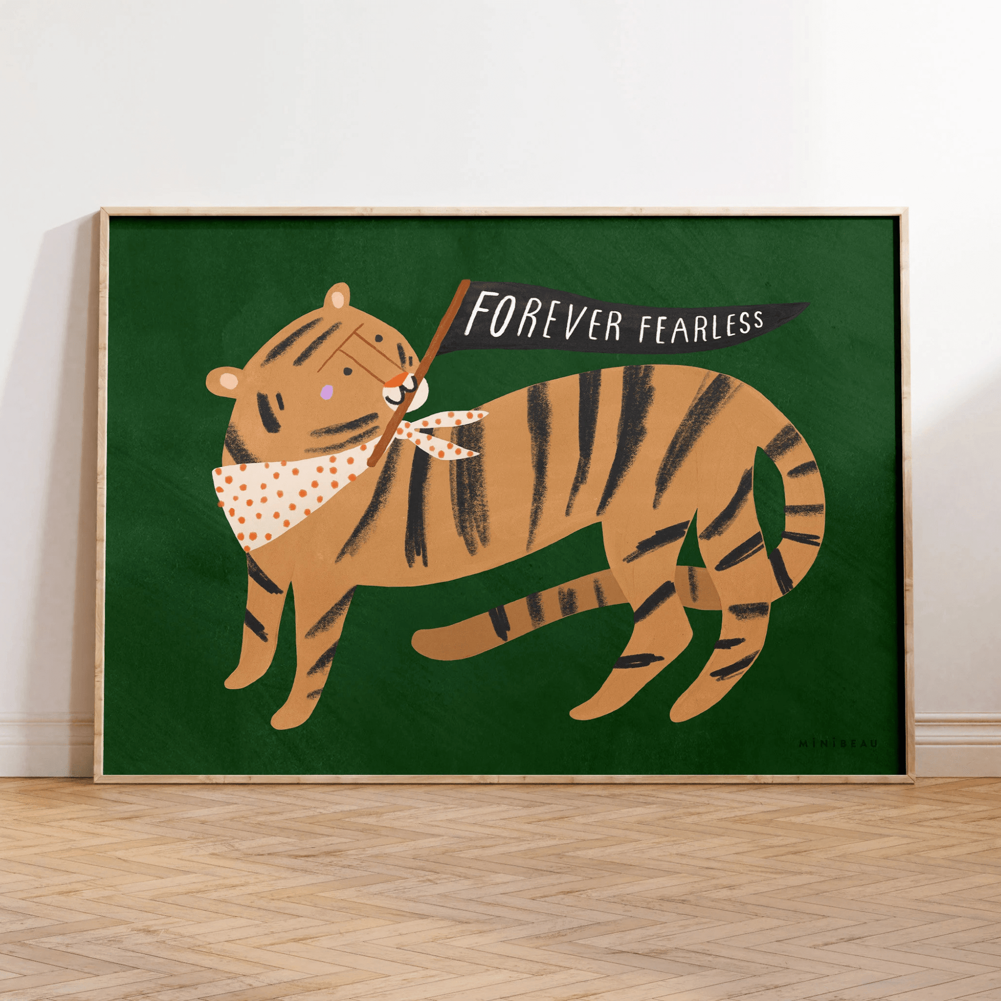 Art print in a light wood frame, leaning against a neutralwall, standing on parque flooring. Our forever fearless art print features a smiling tiger wearing a white bandana with orange polka dots. It's head is turned over it's shoulder and it is holding a black triangle flag with the words FOREVER FEARLESS in white, it it's mouth. All on a green background.