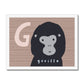 Art print in a white frame. Art print in a light wood frame, leaning against a white wall, standing on parquet flooring. Our G is for Gorilla art print features a smiling cartoon gorilla from the shoulders up, on a brown wood effect background with a large G in a pale brown next to the Gorilla's head.