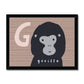 Art print in a black frame. Art print in a light wood frame, leaning against a white wall, standing on parquet flooring. Our G is for Gorilla art print features a smiling cartoon gorilla from the shoulders up, on a brown wood effect background with a large G in a pale brown next to the Gorilla's head.