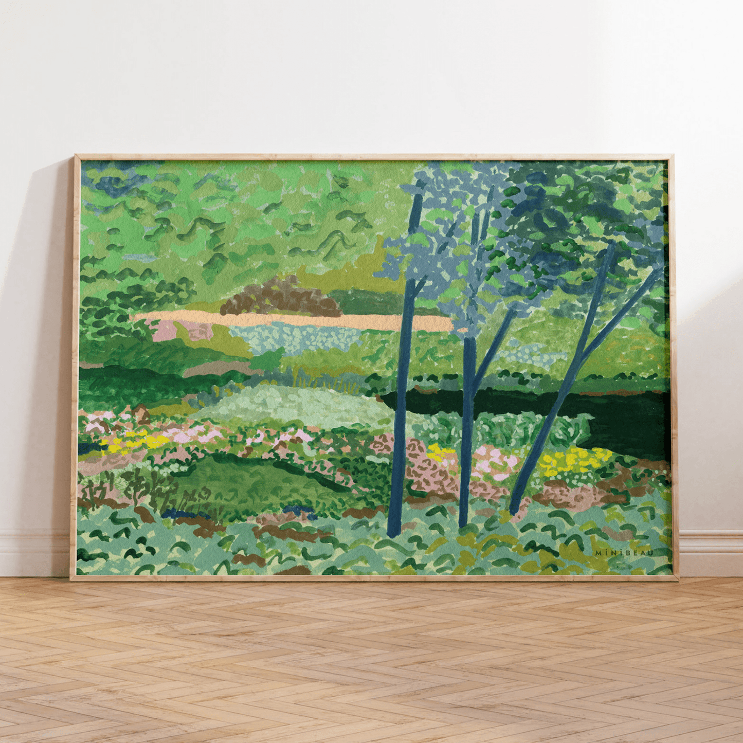 Art print in a light wood frame leaning on a white wall, standing on a parquet floor. Our Garden art print shows a beautiful painted country scene, a winding green path through floral meadows and woodland with a lake to the side, The print is green with tones of pink and yellow to represent flowers.