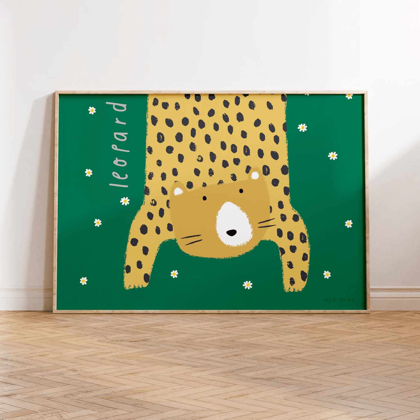 Our Leopard art print in a wooden frame leaning against a white wall, standing on parquet flooring. Hand-drawn leopard hanging down in to the picture, lifting it's head to look out at us on a green background with daisies falling.