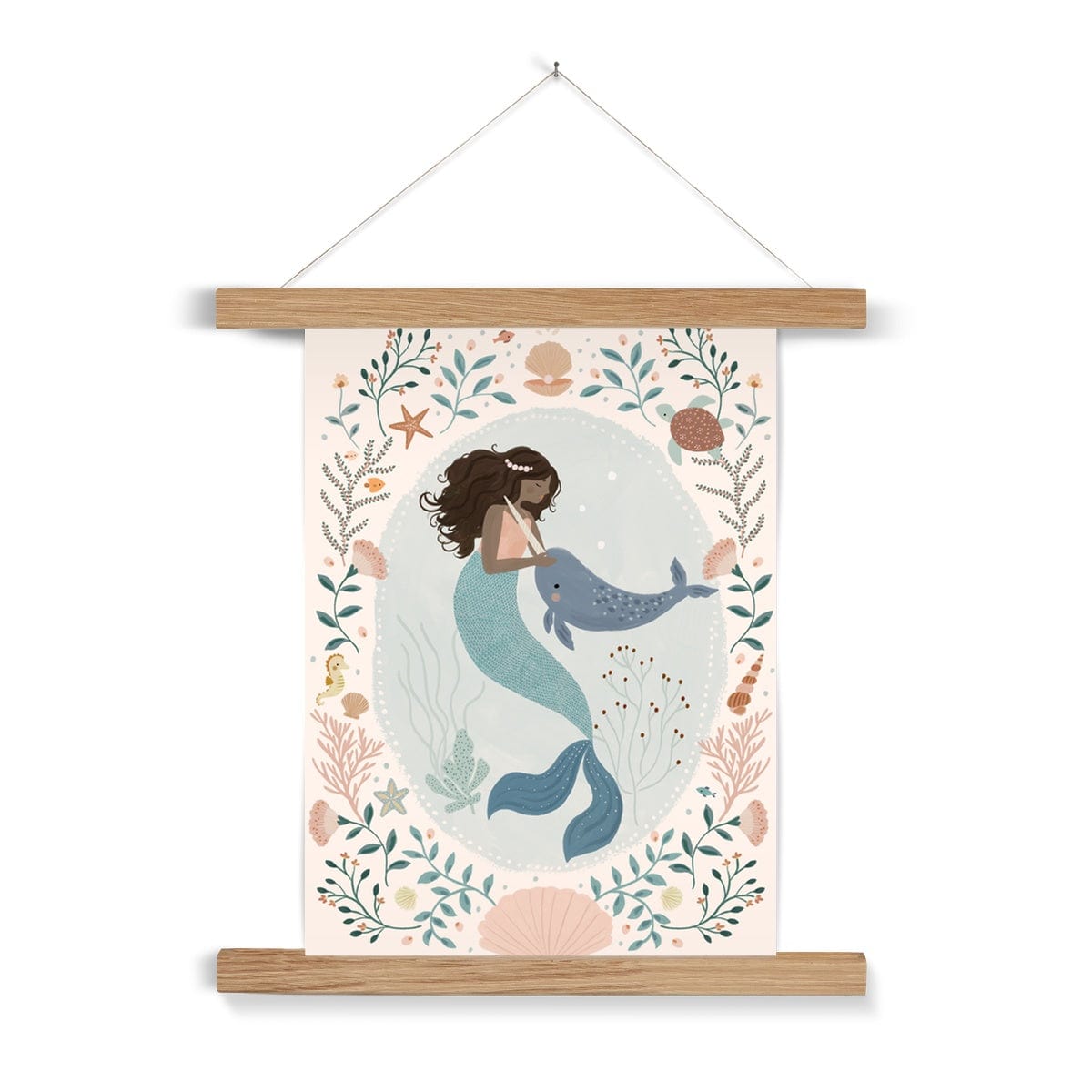 Beautiful dark skinned and haired mermaid with a pearl headband petting her friend Narwhal within a pale teal coloured oval background with white dots round the edge. On the outside of the oval is a sea themed border on a neutral background. The border consists of foliage, flowers and items you would find at the bottom of the sea, shells, turtle, sea horse with a large clam shell at the bottom, hanging from a nail in a natural wooden hanger