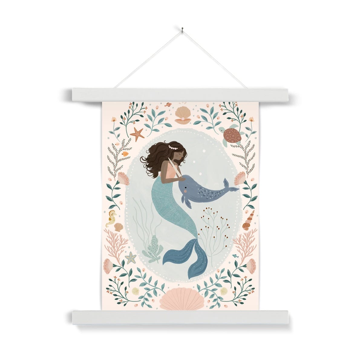 Beautiful dark skinned and haired mermaid with a pearl headband petting her friend Narwhal within a pale teal coloured oval background with white dots round the edge. On the outside of the oval is a sea themed border on a neutral background. The border consists of foliage, flowers and items you would find at the bottom of the sea, shells, turtle, sea horse with a large clam shell at the bottom, hanging from a nail in a white wooden hanger