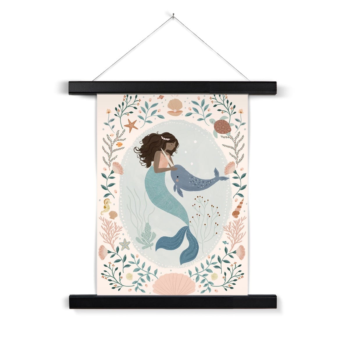 Beautiful dark skinned and haired mermaid with a pearl headband petting her friend Narwhal within a pale teal coloured oval background with white dots round the edge. On the outside of the oval is a sea themed border on a neutral background. The border consists of foliage, flowers and items you would find at the bottom of the sea, shells, turtle, sea horse with a large clam shell at the bottom, hanging from a nail in a black wooden hanger