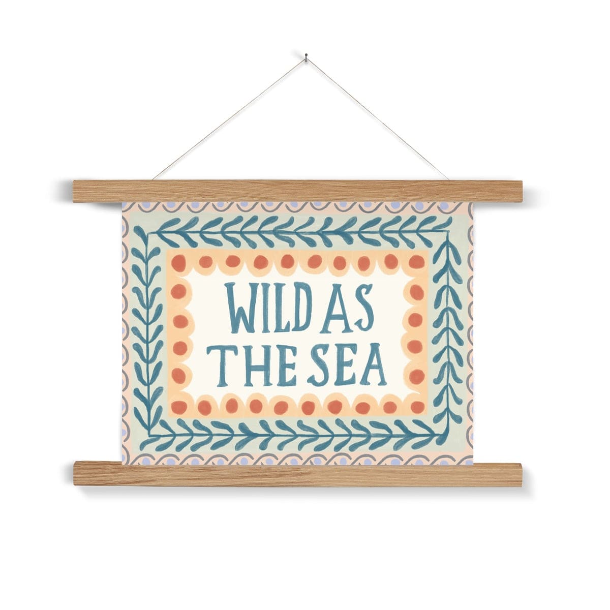 A typography print with the words WILD AS THE SEA in capital letters in watercolour deep teal in the middle on a neutral background, with 3 borders. The first being yellow scallops with deep orange dots, the second being foliage in the same colour as the typography on a pale green background and the outer being a sage wave pattern with lilac dots on a peach background, hanging from a nail in a natural wood hanger