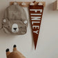 Kids teddy bear back pack hanging from a peg rail with cloud peg next to a brown pennant with white writing saying FINLEY