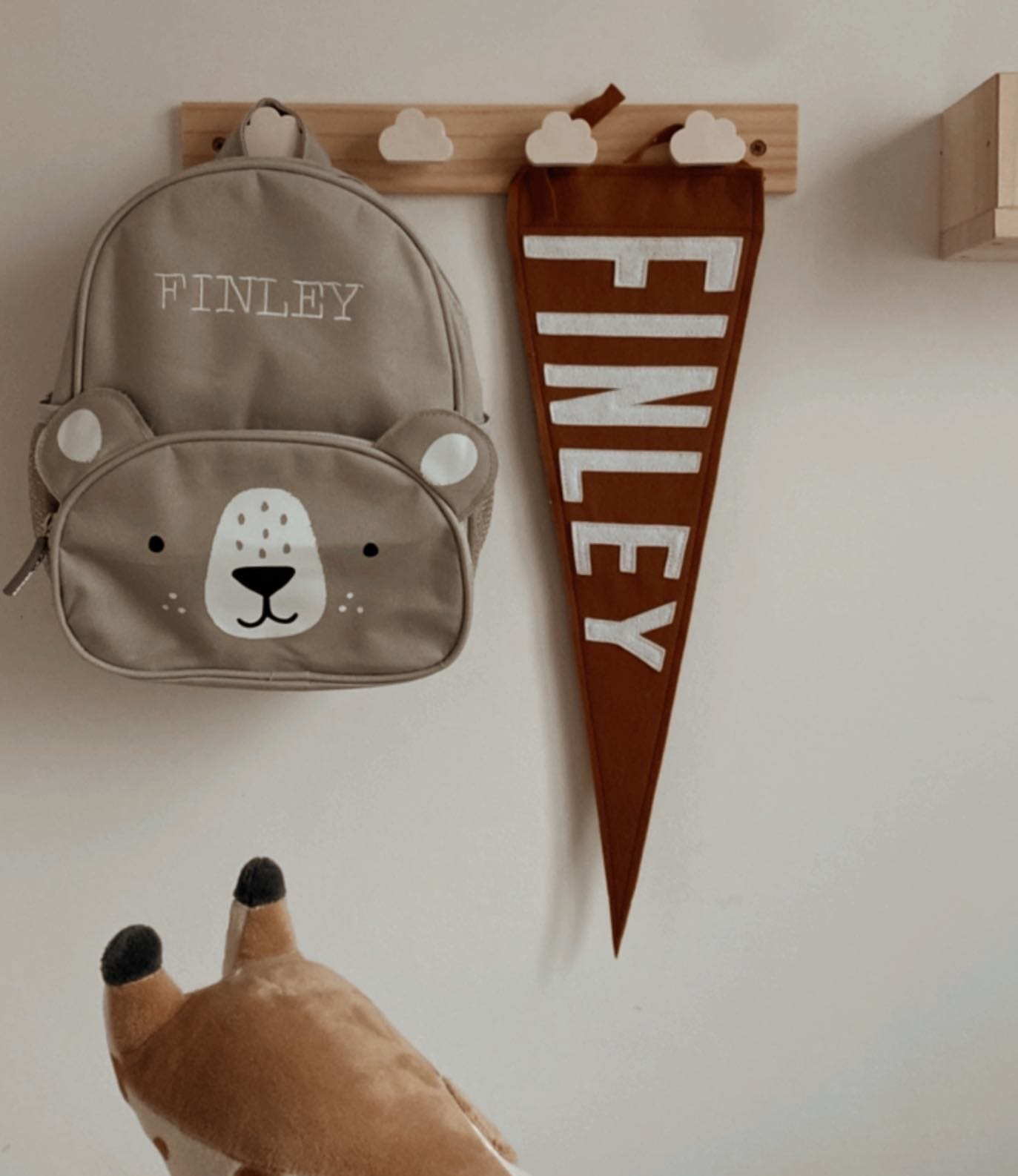 Kids teddy bear back pack hanging from a peg rail with cloud peg next to a brown pennant with white writing saying FINLEY