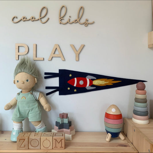 Space rocket pennant on the wall under a wooden play sign. Over a wooden unit with a wooden stacking rocket and wooden blocks spelling out ZOOM