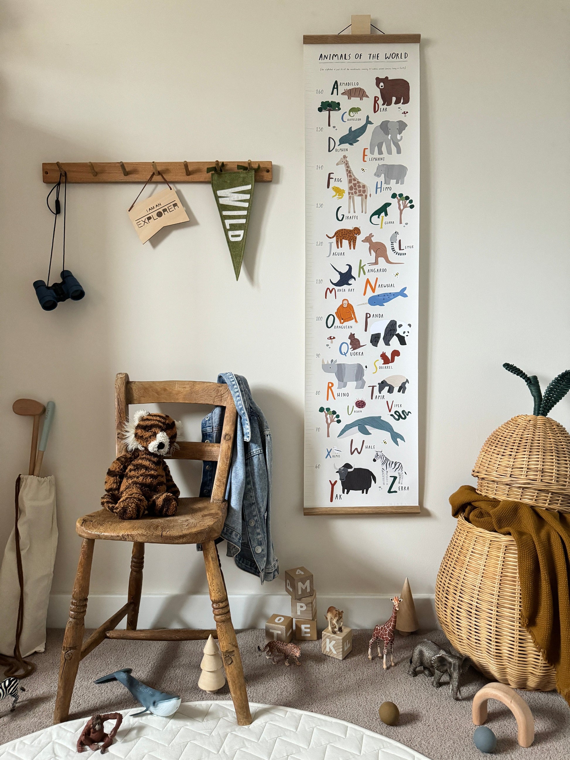 Animals of the world height chart hanging from a square wooden hook, next to a vintage wood coat hook rail, with a vintage wooden chair underneath with a plush tiger on, Shleich animals are on the floor with wooden alphabet blocks