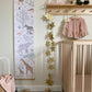 Our Serengeti height chart with oak hanger hung from a round wooden hook on a wall next to a cot with a star garland hanging down from a shelf with hooks underneath. On the shelf is a hello kiddo hello sign, a plush panda and some blocks