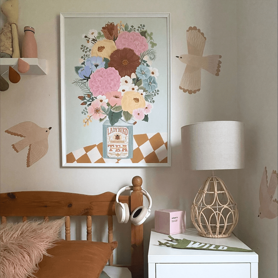 The corner of a childs bedroom with a wooden framed bed with headphones hung on the bedpost. A large Minibeau boho floral vase art print in a white frame with three bird stickers on the walls.
