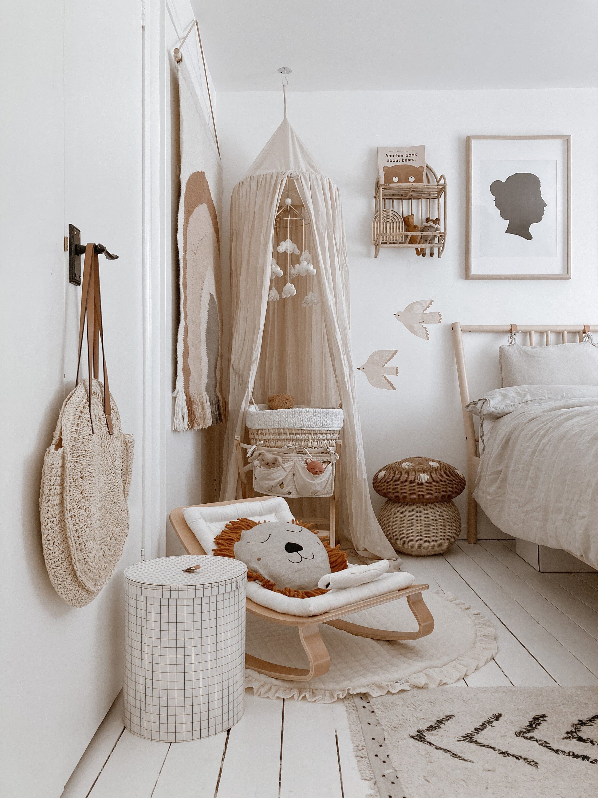 Showing a busy corner of a neutral bedroom with a bamboo framed bed and charlie crane baby rocker and a cream canopy, with 2 of the bird stickers on the wall next to the bed.