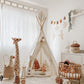 A corner of a child room featuring a white teepee, an olli ella luggy, a kids concept guitar a rattan crib and the four Murs Clairs bird wall stickers on the wall