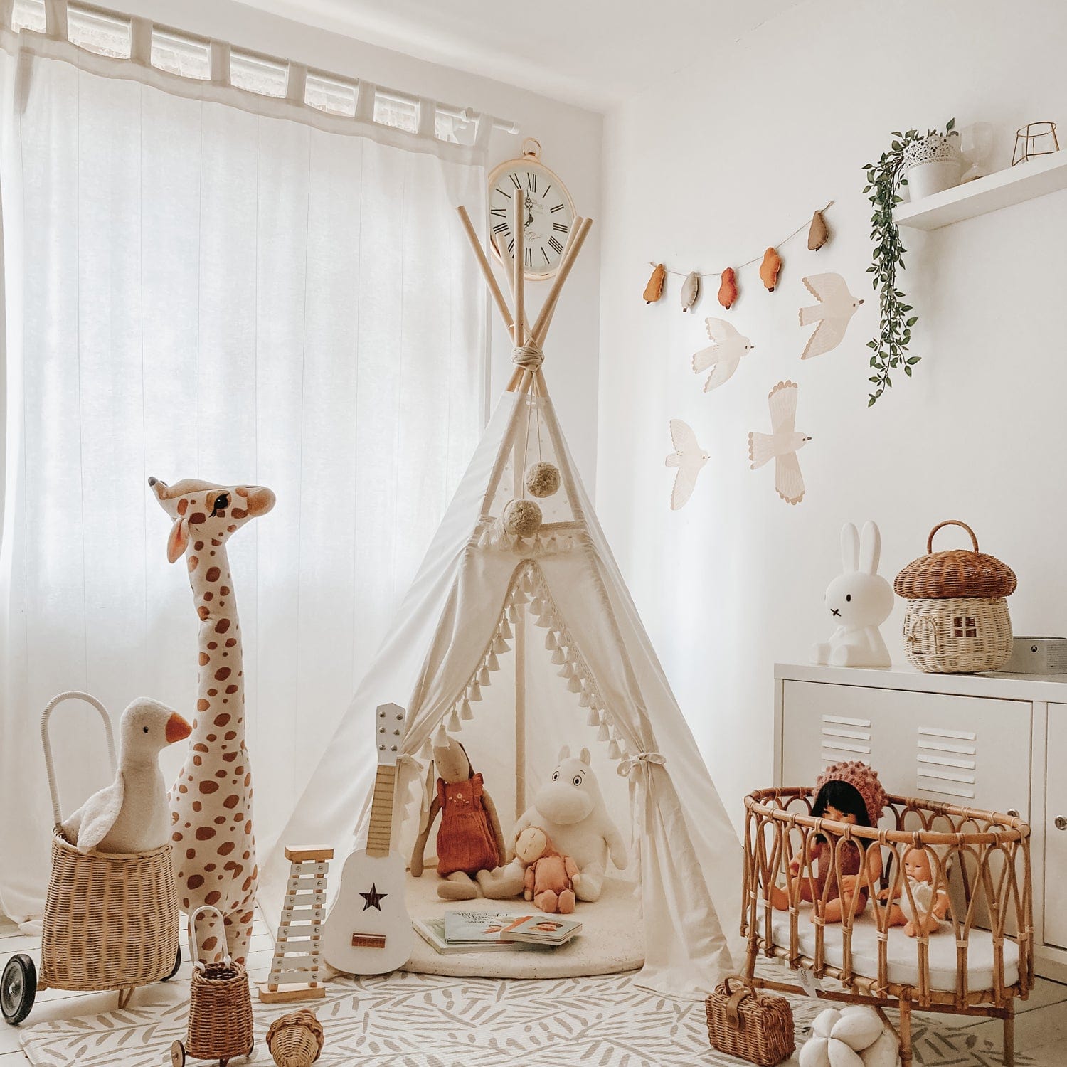 A corner of a child room featuring a white teepee, an olli ella luggy, a kids concept guitar a rattan crib and the four Murs Clairs bird wall stickers on the wall