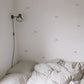 Photo of the corner of a bedroom showing part of an unmade bed with a black lamp and grey cloud wall stickers on the wall
