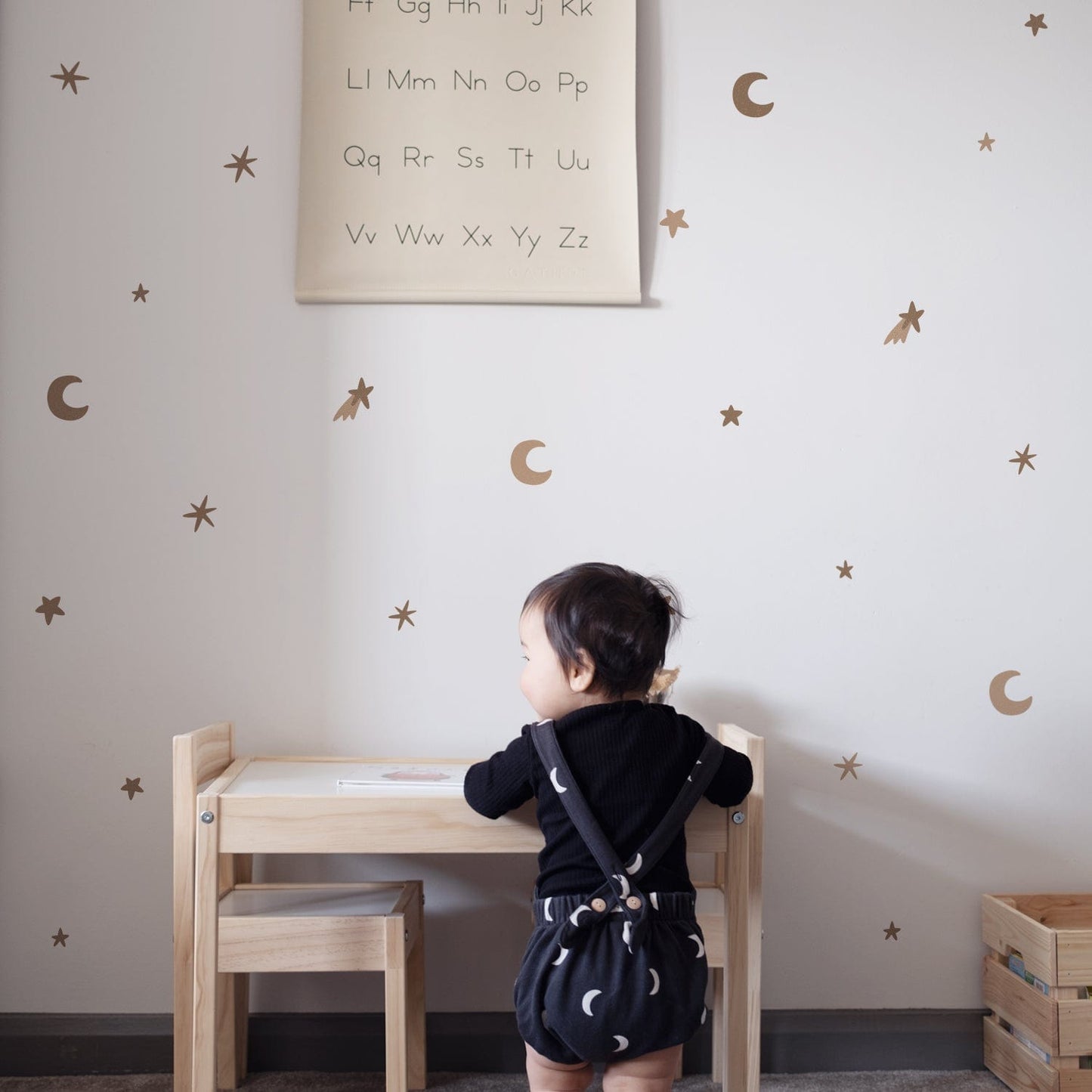 Toddler standing at a childs ikea table in frony of a white wall with sand star and cloud stickers on them.