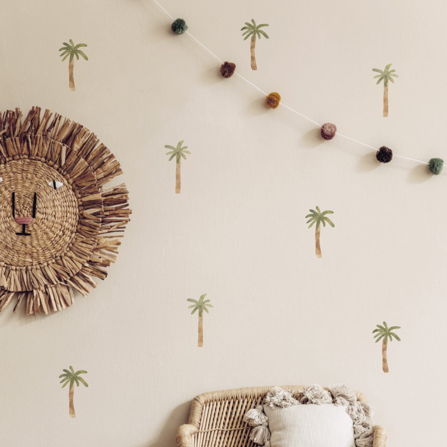 Palm tree wall stickers on a neutral wall, with a pom pom garland and a Bloomimgville basir lion wall decoration, with a rattan chair to the bottom of the photo