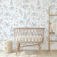 Wallpaper of delicate line work animals in blue such as mummy and baby elephants, mummy and baby pandas and mummy and baby koalas, tigers, elephants and giraffes on a neutral background with fir leaf detail behind a vintage rattan crib and fabric pop pop storage basket